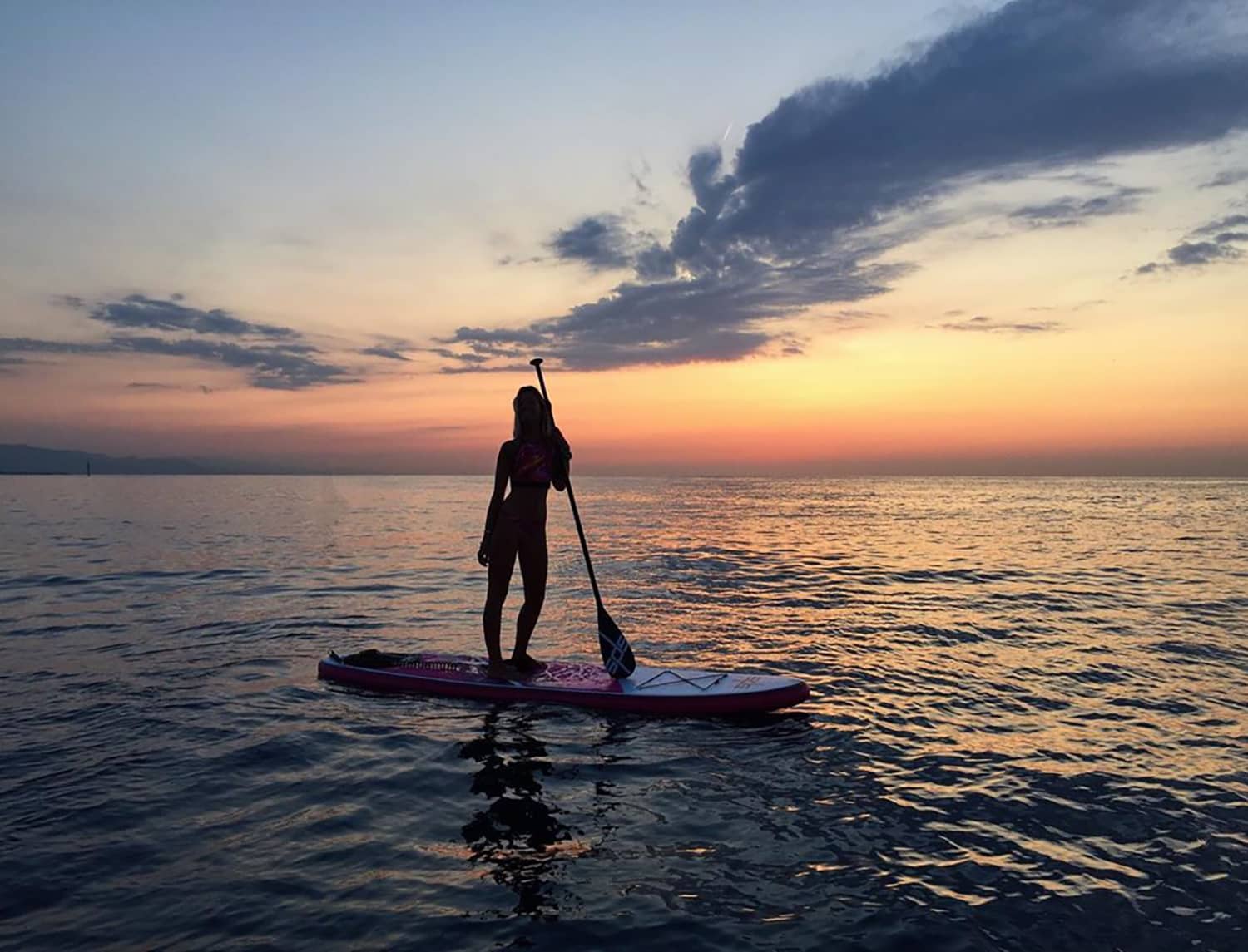 Chica remando en el mar con una tabla Evo Rosa durante el anochecer